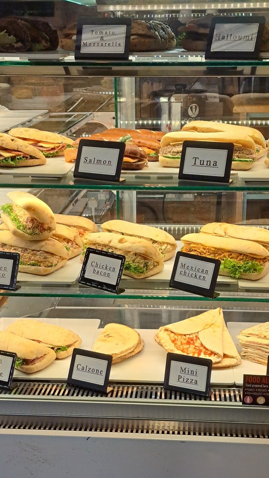 Tall chilled deli cabinet stacked with filled baguettes, sandwiches and focaccia