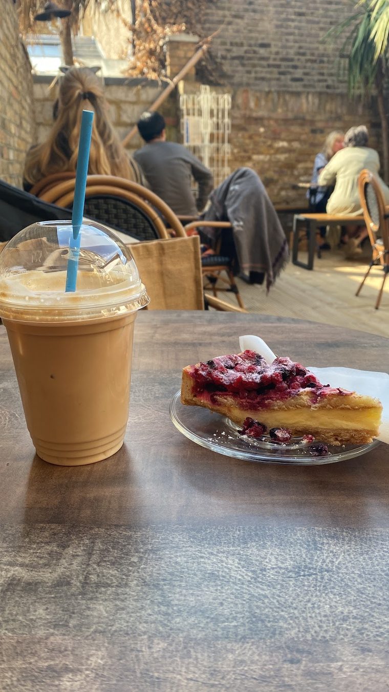 Iced coffee in a tall cup beside a berry-topped tart